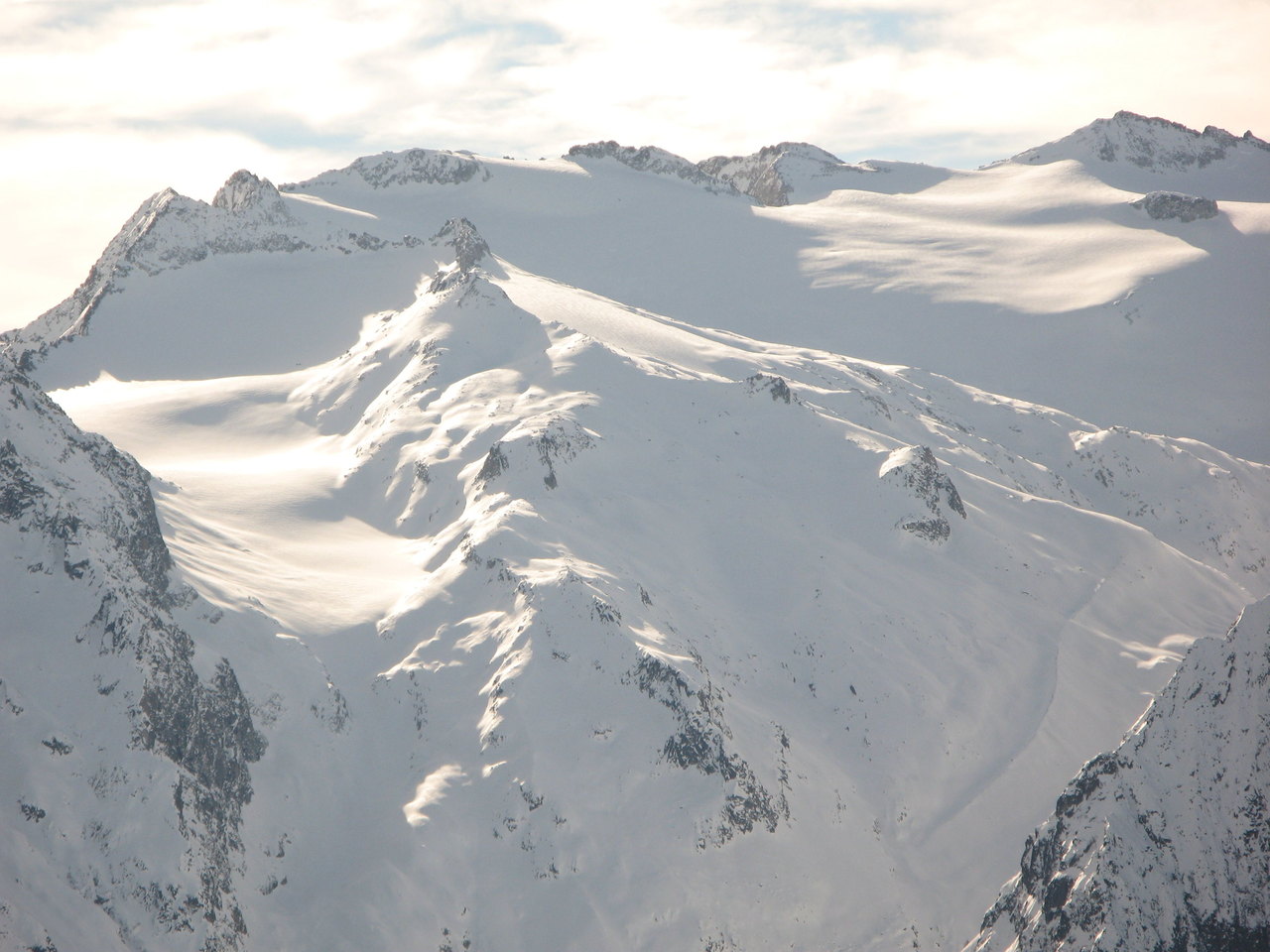 La sommità innevata del monte Adamello con la calotta glaciale e le creste rocciose che ne delimitano il versante.