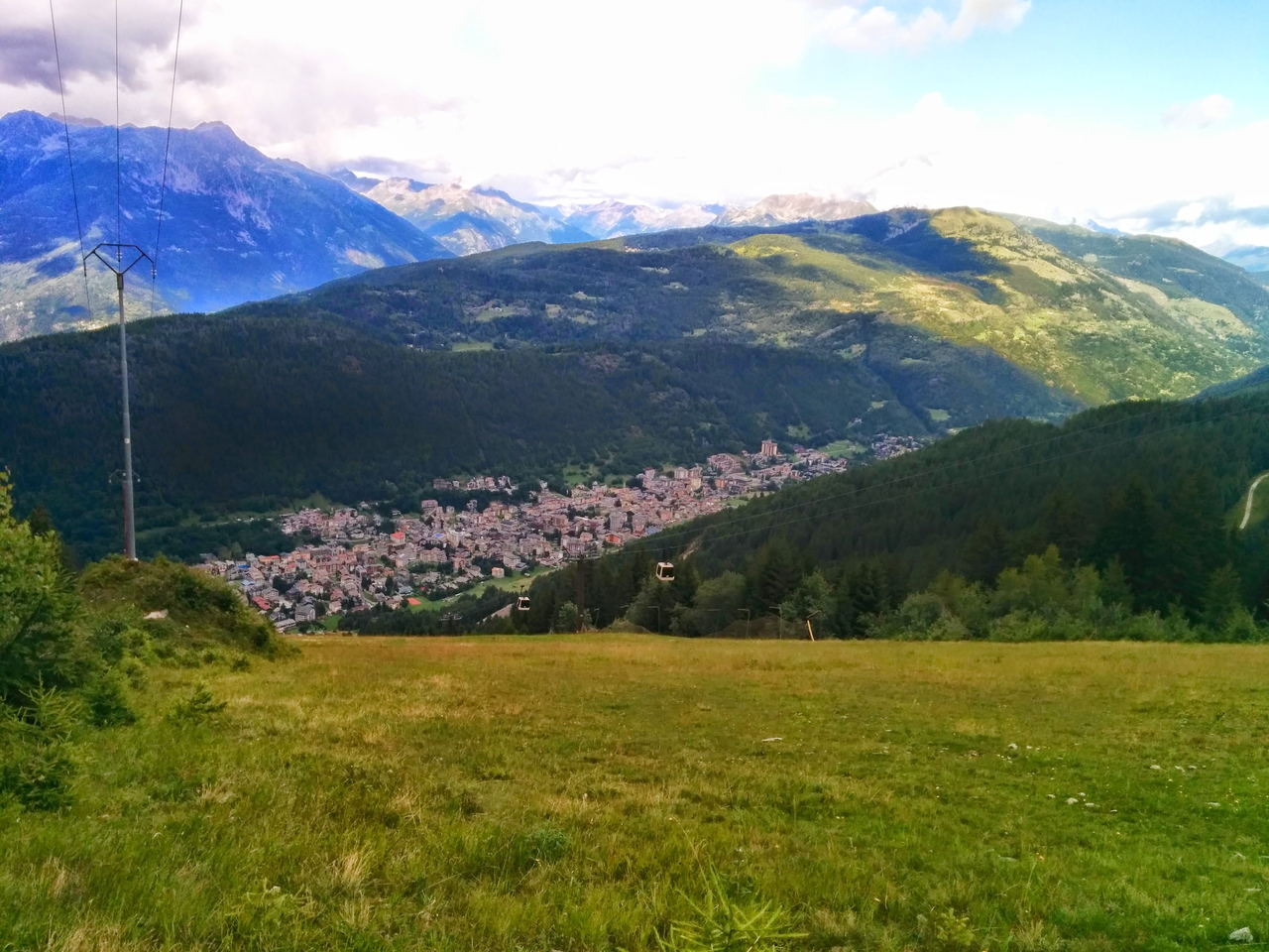 Prati da sfalcio e boschi sopra Aprica, con il fondovalle e le montagne che chiudono l'orizzonte.
