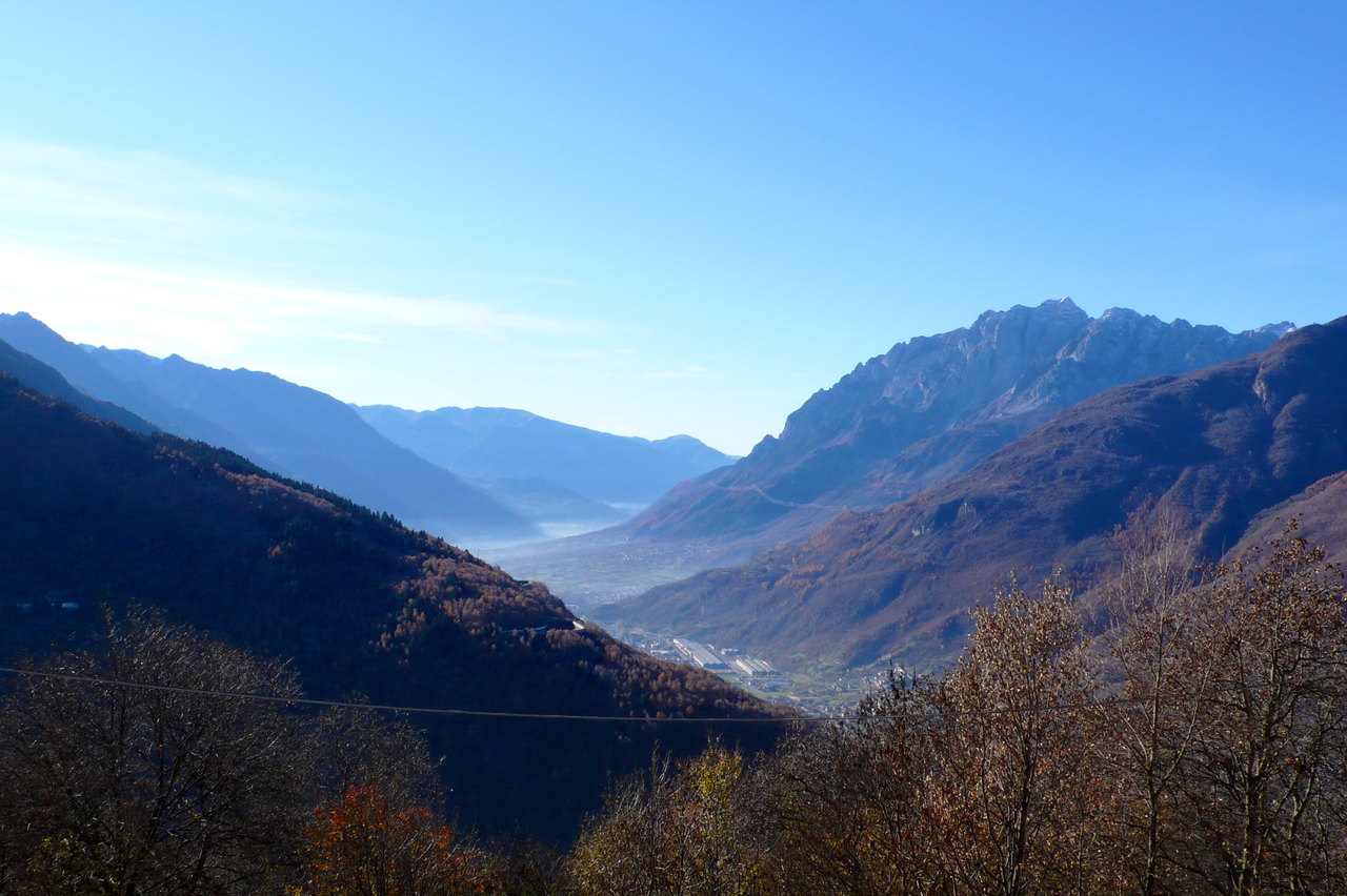 Veduta dall'alto della Valcamonica da Cevo, con i versanti boscosi che scendono al fondovalle e le montagne in lontananza.