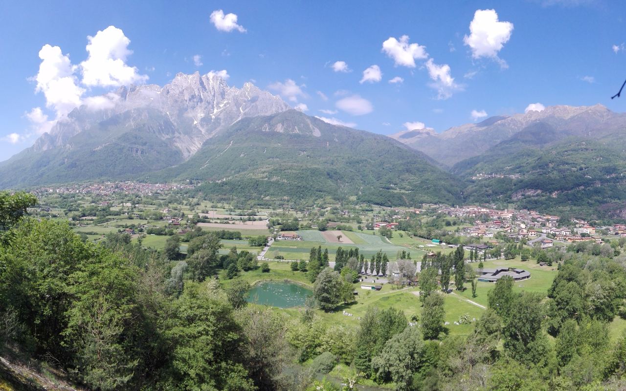 La Concarena si alza sopra il fondovalle coltivato, con l'abitato di Capo di Ponte disteso alla sua destra e un piccolo lago fra gli alberi in primo piano.