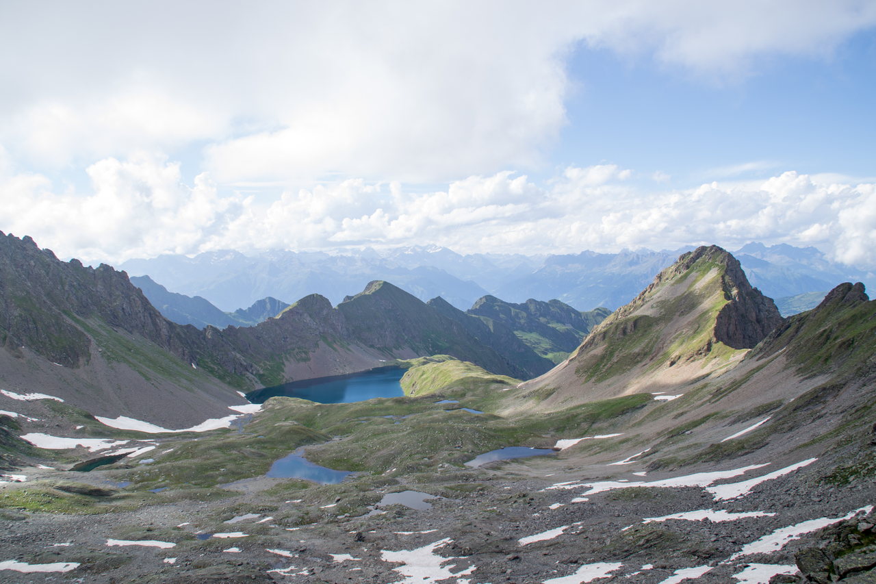 Un piccolo lago alpino in una conca rocciosa dell'alta Val Brandet, con residui di neve sui versanti e le cime attorno.