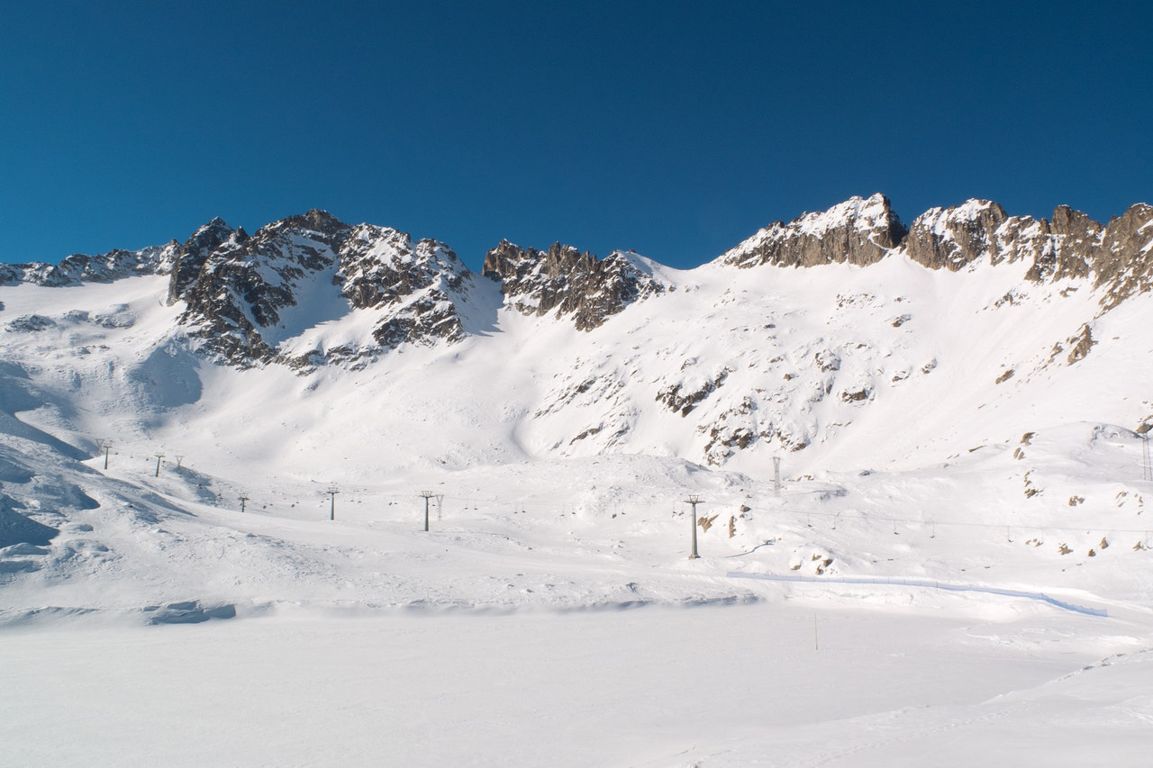 Il ghiacciaio Presena innevato, con i piloni degli impianti di risalita che attraversano il pianoro glaciale e le cime rocciose sullo sfondo.