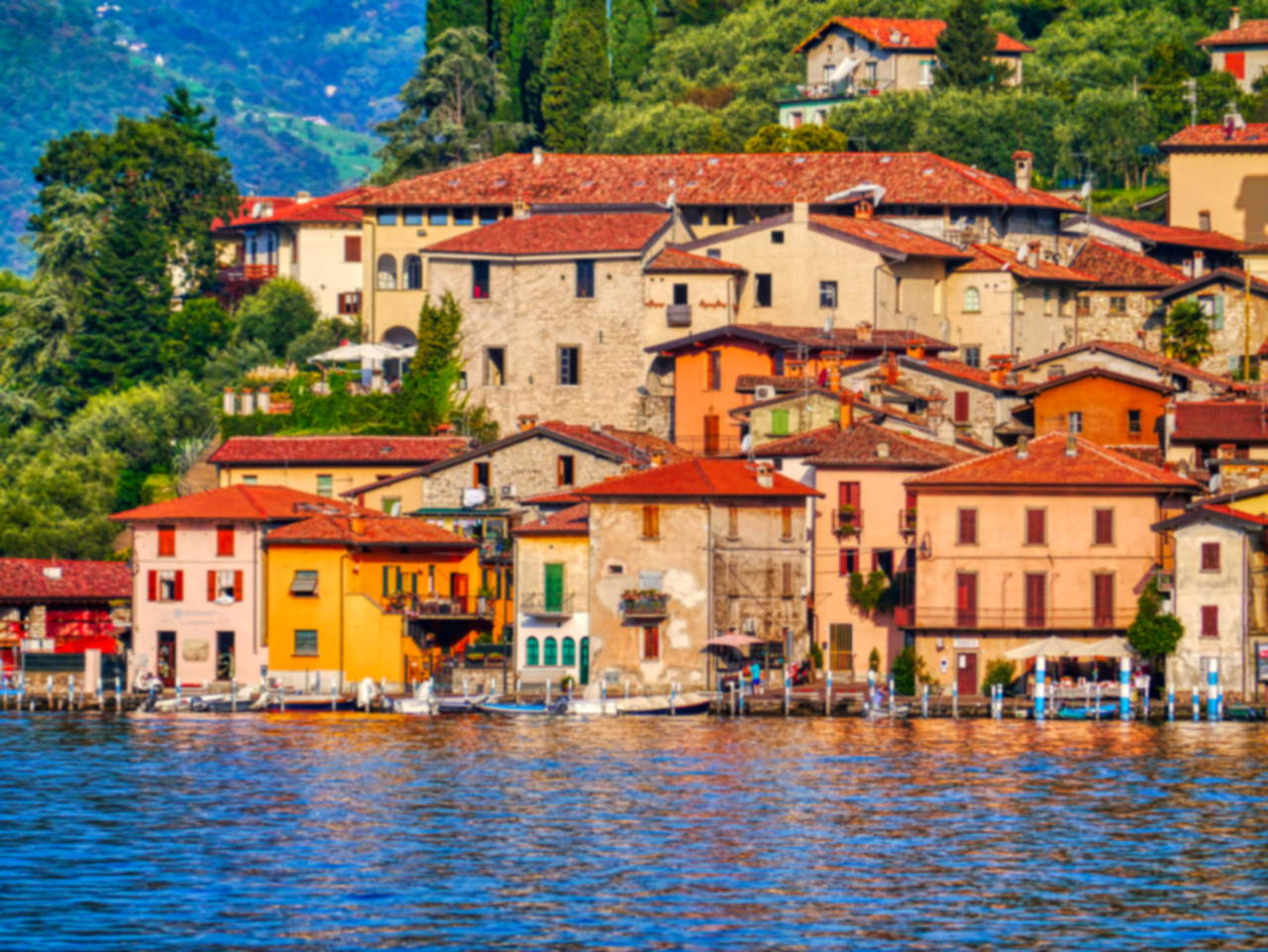 Le case colorate di Peschiera Maraglio affacciate sull'acqua del lago d'Iseo, con barche ormeggiate lungo la riva.