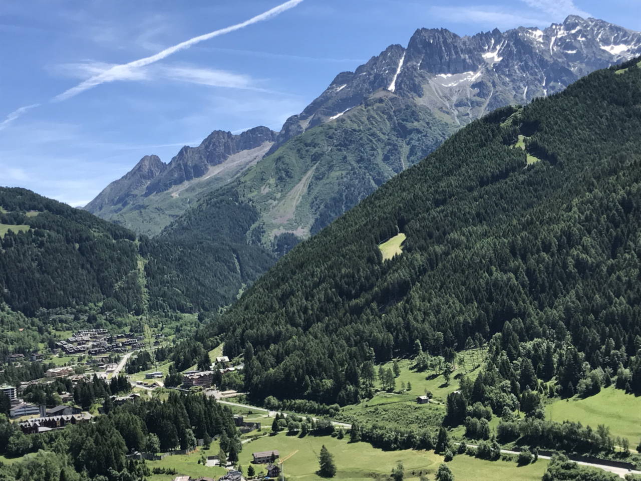 Veduta dall'alto di Ponte di Legno nel fondovalle, con le case raccolte attorno al centro e i versanti boscosi che salgono ai lati.