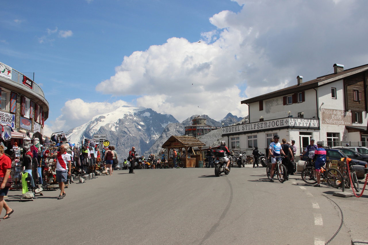 Il piazzale sommitale del Passo dello Stelvio in estate: auto e motociclette in transito, alberghi e banchi lungo la strada, il ghiacciaio sullo sfondo.
