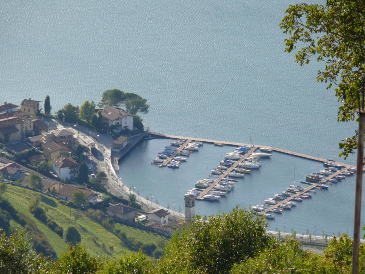 Veduta dall'alto del porto di Pisogne e della sponda settentrionale del lago d'Iseo, con i pontili e le barche ormeggiate.