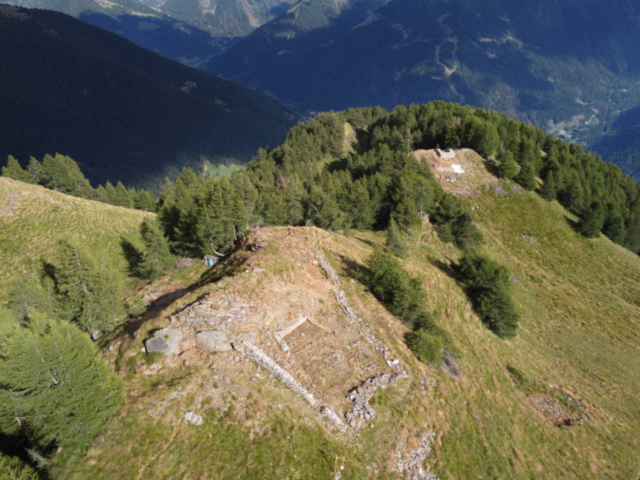 I ruderi in pietra del Tor dei Pagà su un dosso erboso, visti da nord-ovest, con i versanti della valle sullo sfondo.